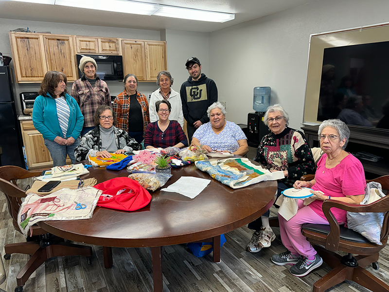 San Luis Stitching Group, 2024. Left to right standing: Julia Mondragon, Connie Mamich Morrell, Aurora Martinez, Marcella Pacheco, Trent Segura. Left to right sitting: Maria Eufemia Barela, Susan Walanski, Donna Madrid Hernandez, Irene Medina, and Mary Vigil de Rodriguez.